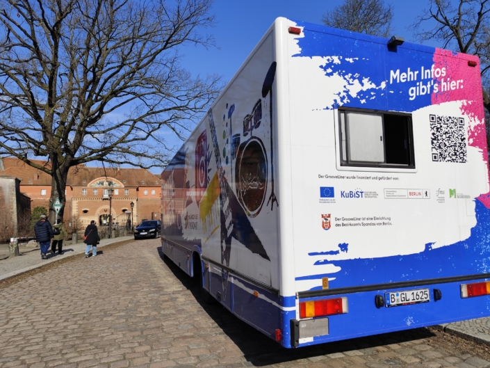 grooveliner-1 weißblauer Bus vor Gebäude